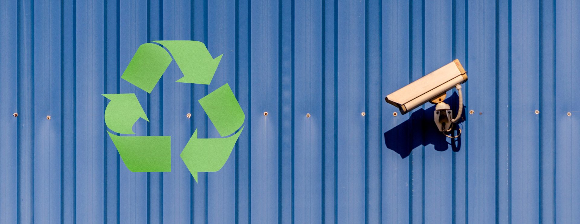 Eine Überwachungskamera an einer blauen Wand ist auf das Recycling-Symbol gerichtet