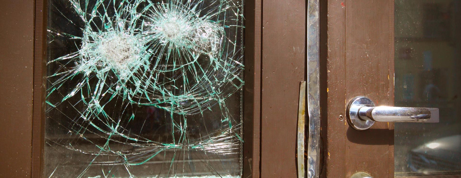 Eine braune Holztür mit eingeschlagener Scheibe und aufgehebeltem Schloss