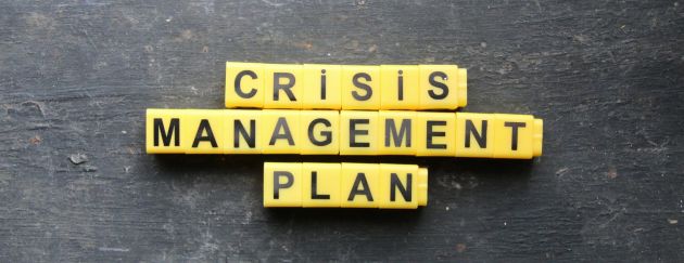 Auf einem schwarzen Hintergrund liegen viele kleine geordnete Plättchen auf denen jeweils ein Buchstabe steht und somit den Begriff „Crisis Management Plan“ zeigen