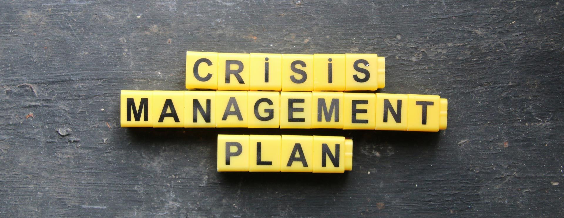 Auf einem schwarzen Hintergrund liegen viele kleine geordnete Plättchen auf denen jeweils ein Buchstabe steht und somit den Begriff „Crisis Management Plan“ zeigen