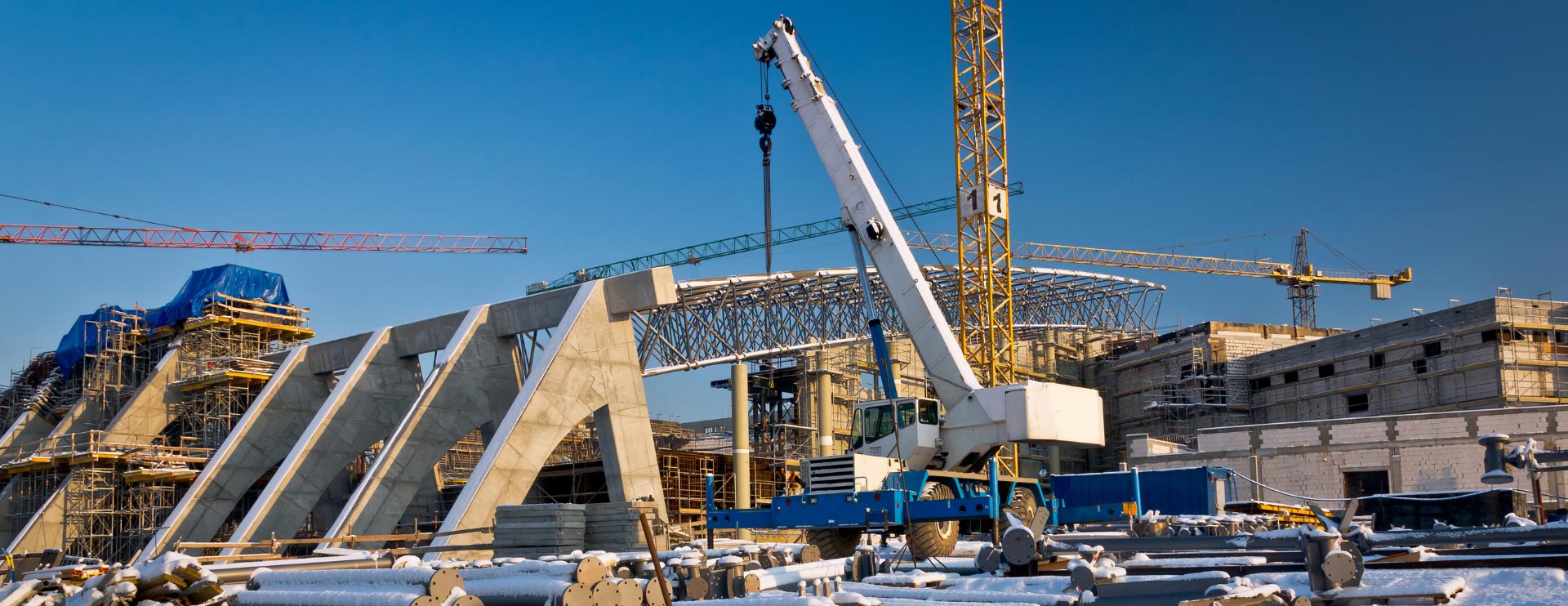 Eine mit Schnee bedeckte Baustelle, mit mehreren Kränen und Konstruktionen bei strahlend blauem Himmel