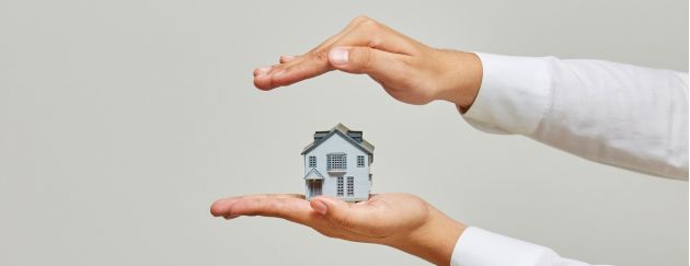 Zwei Hände legen sich schützend um ein kleines Haus.